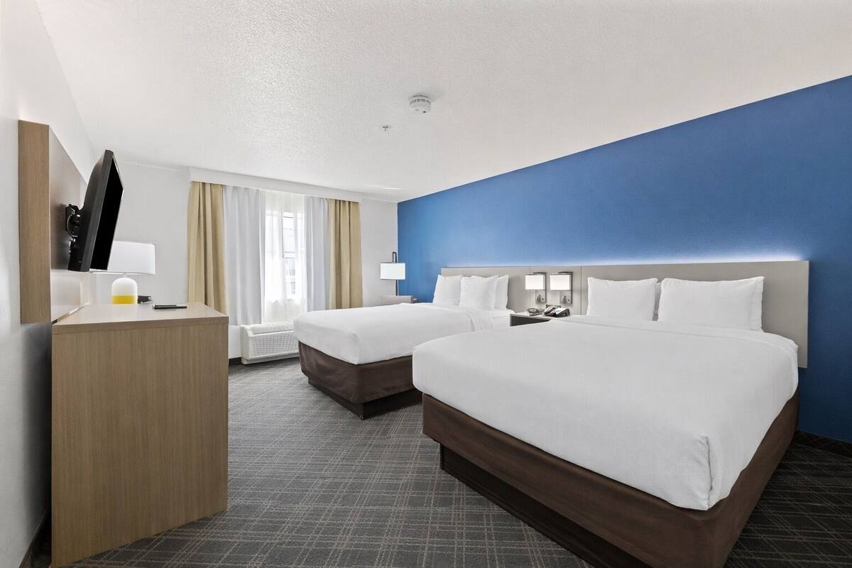 A hotel room with two beds, a desk, a TV, and a window with curtains.