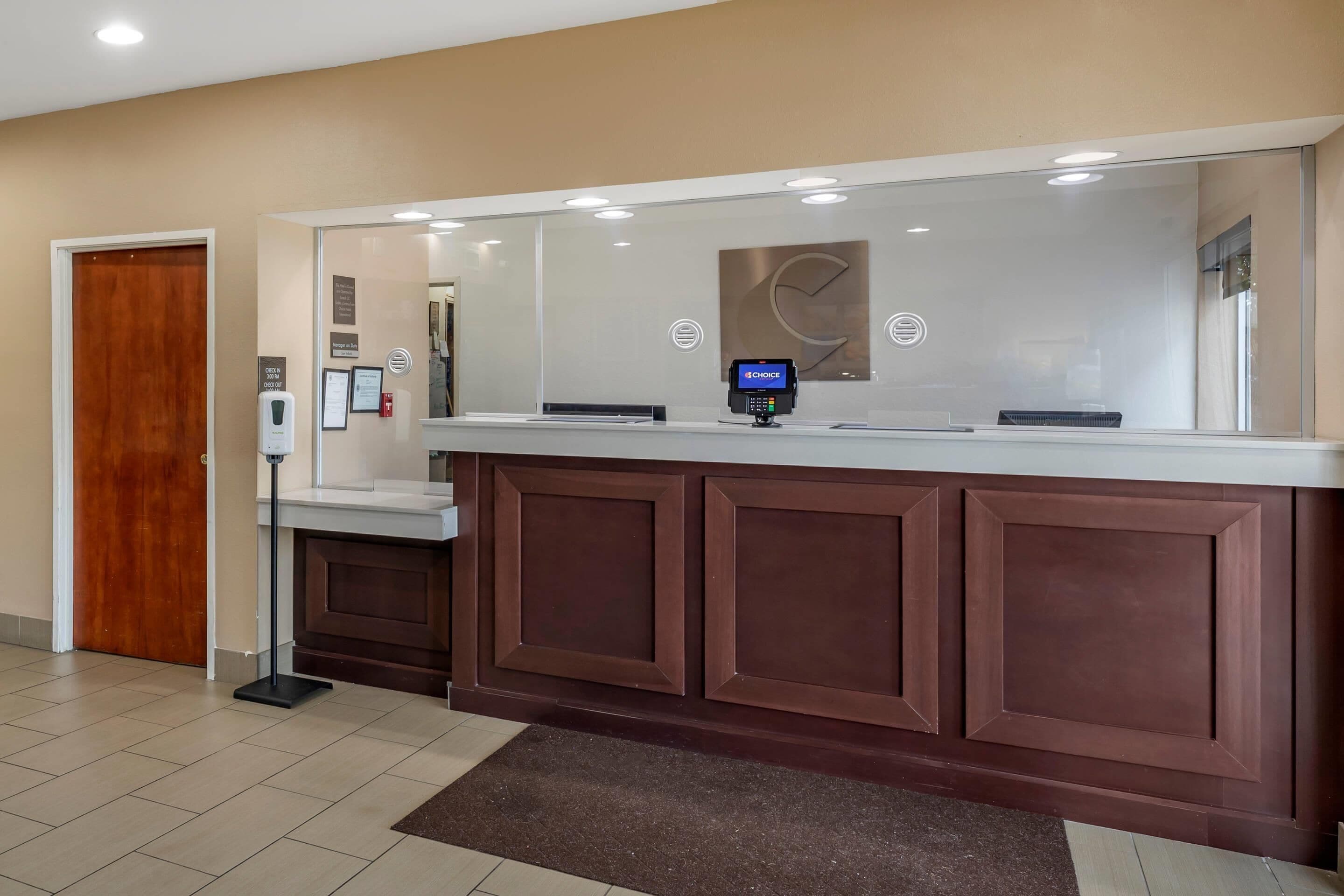 A reception desk with a digital kiosk, a wooden door, and a wall-mounted sign.