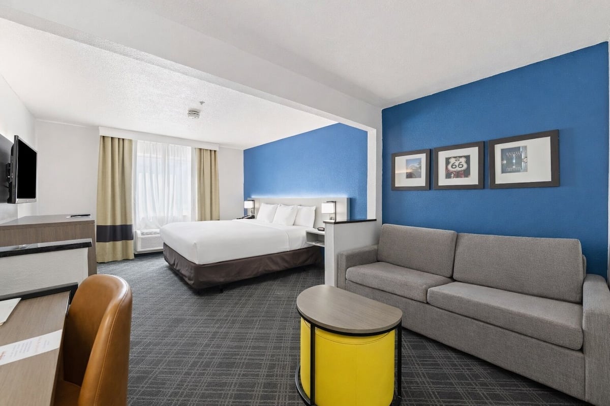 A hotel room with a bed, a sofa, a desk, a chair, and a small table.