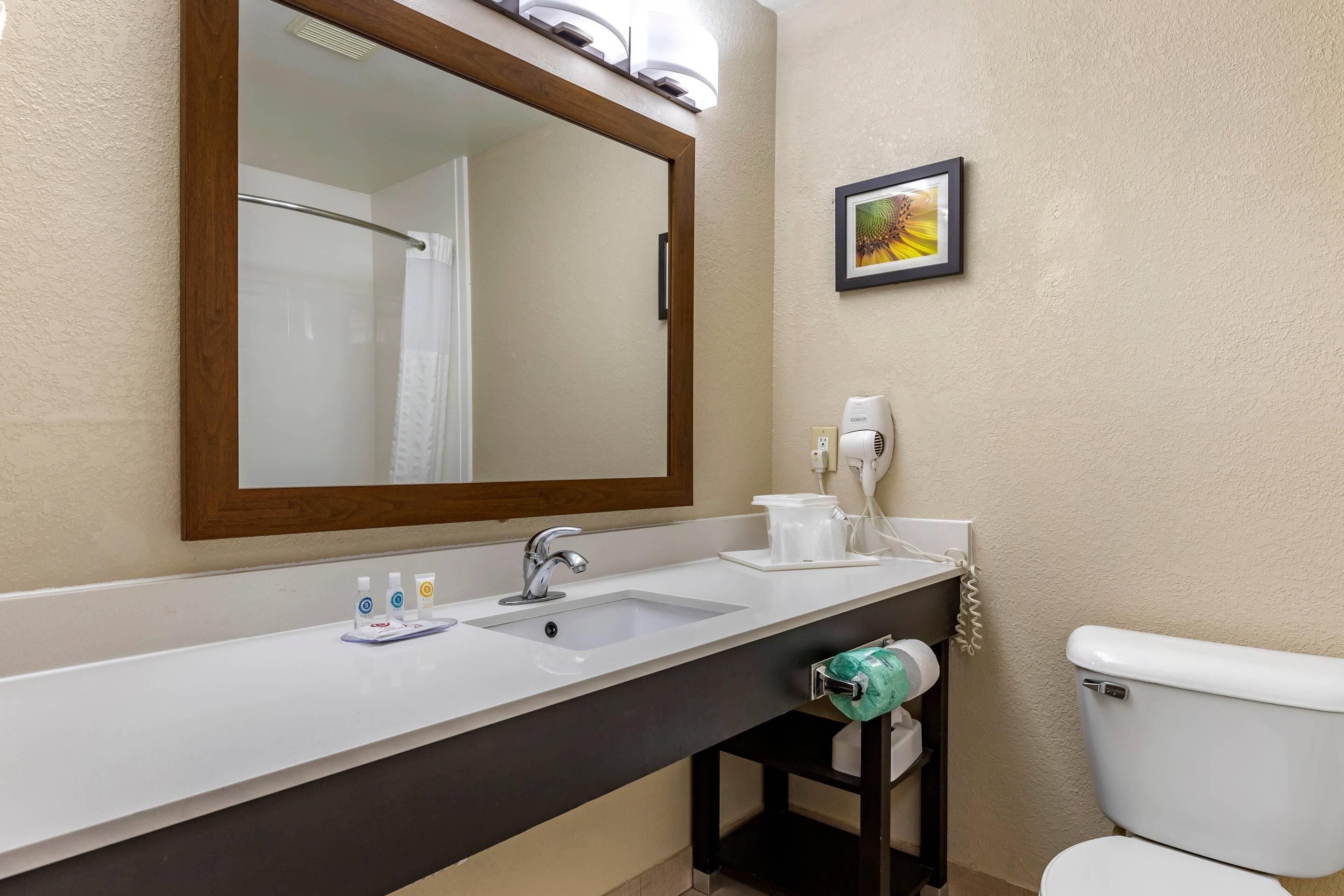 A bathroom with a large mirror, a sink, a toilet, and a towel dispenser.