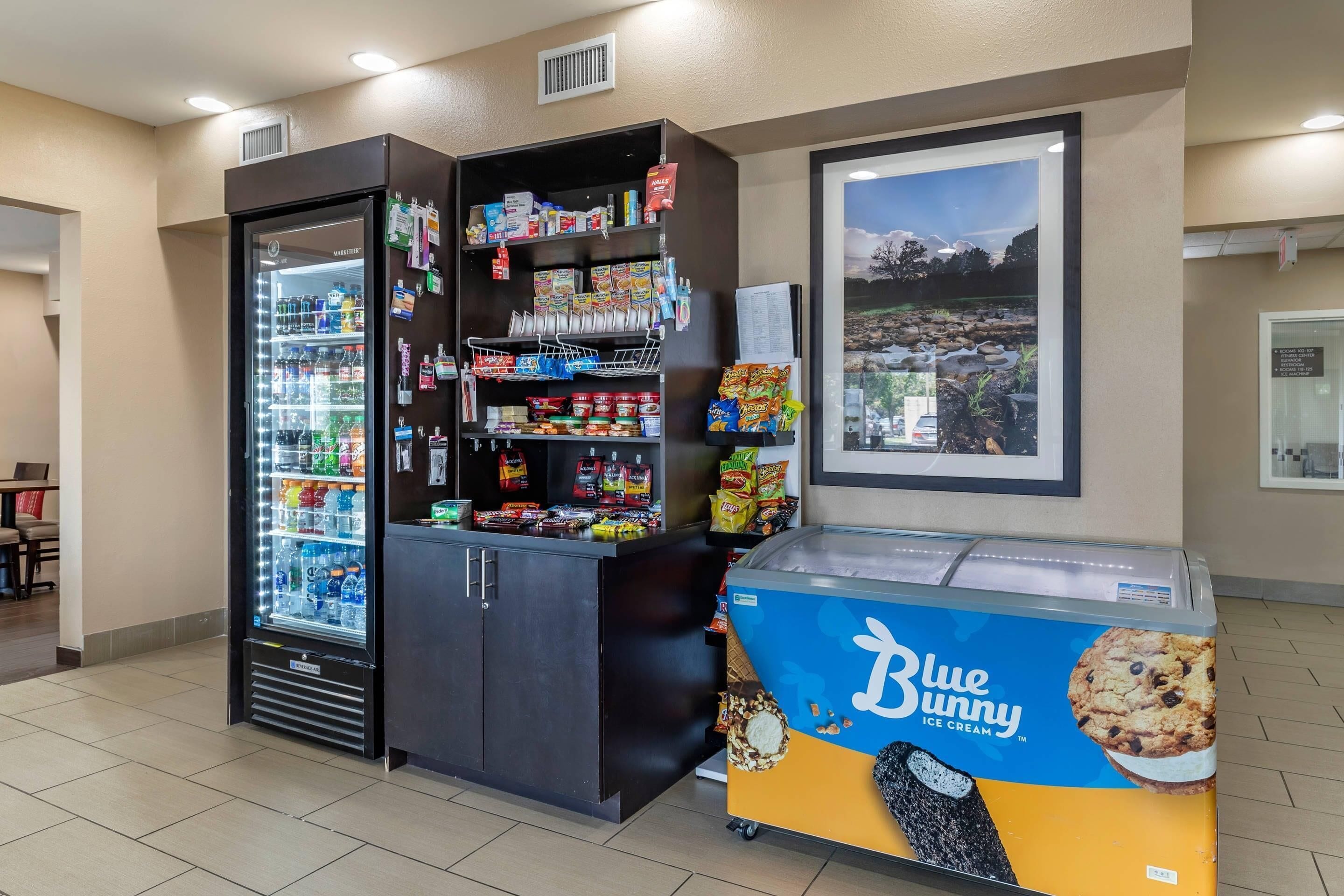 A self-service kiosk with a freezer, shelves stocked with snacks, and a Blue Bunny ice cream display.