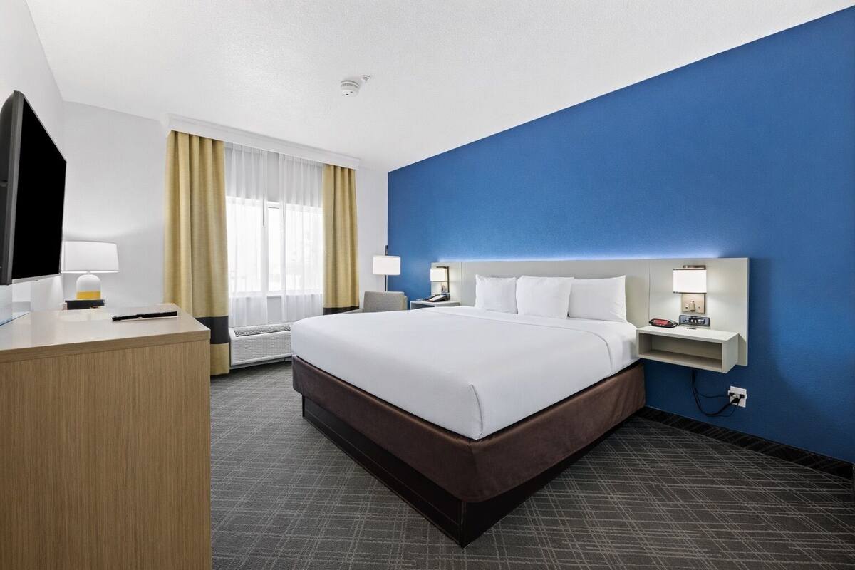 A hotel room with a large bed, a desk, a television, and a nightstand with a lamp.