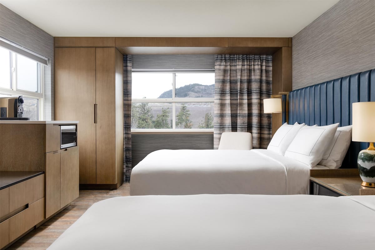 Ett hotellrum med en stor säng, ett skrivbord med en lampa, en garderob och ett fönster med gardiner.