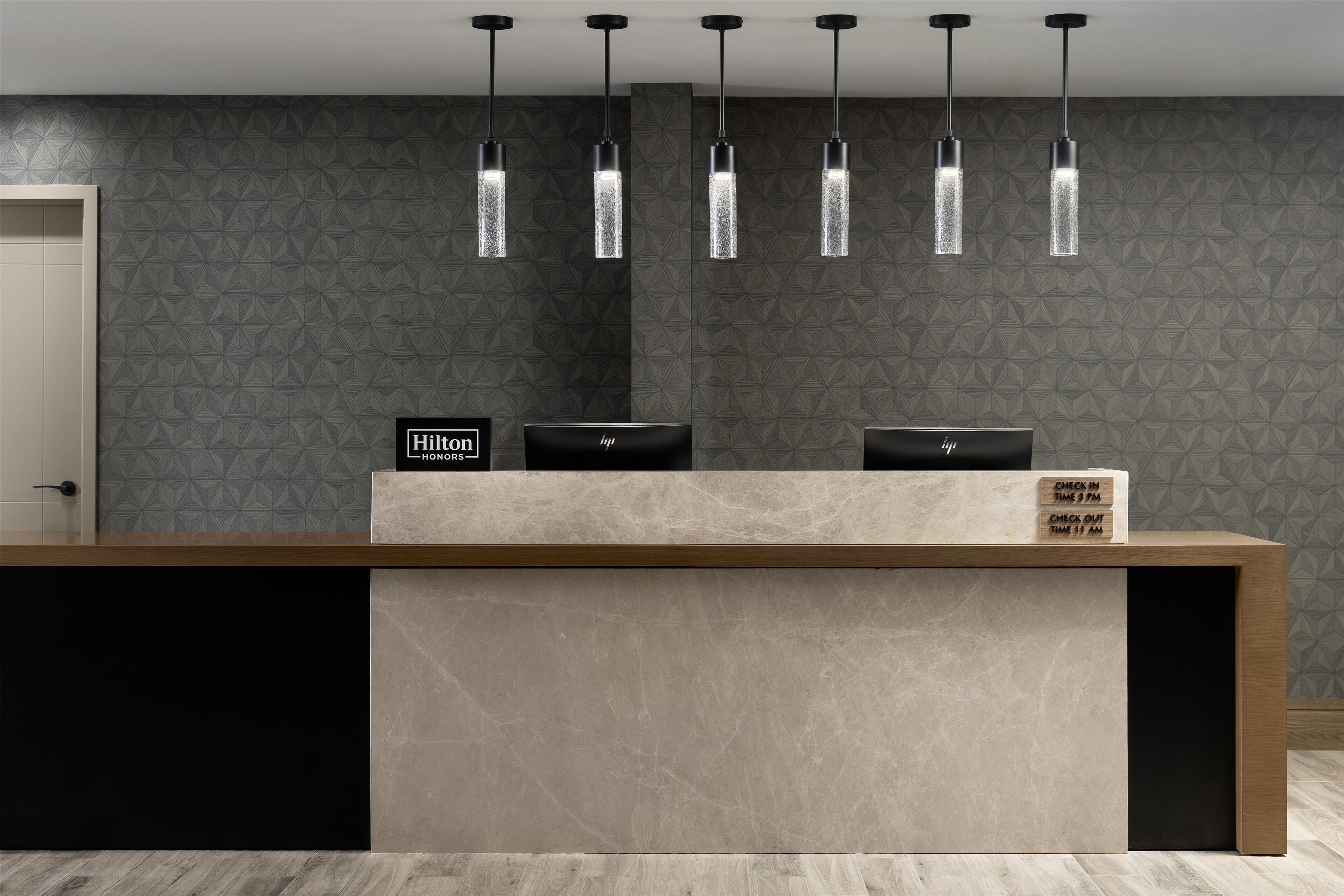 A hotel reception desk with a modern design, featuring a check-in/out sign and a digital display.