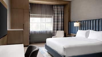 A modern hotel room with a large bed, a desk, a chair, and a TV.