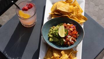 A table with a glass of iced beverage, a bowl of guacamole with lime, and tortilla chips.