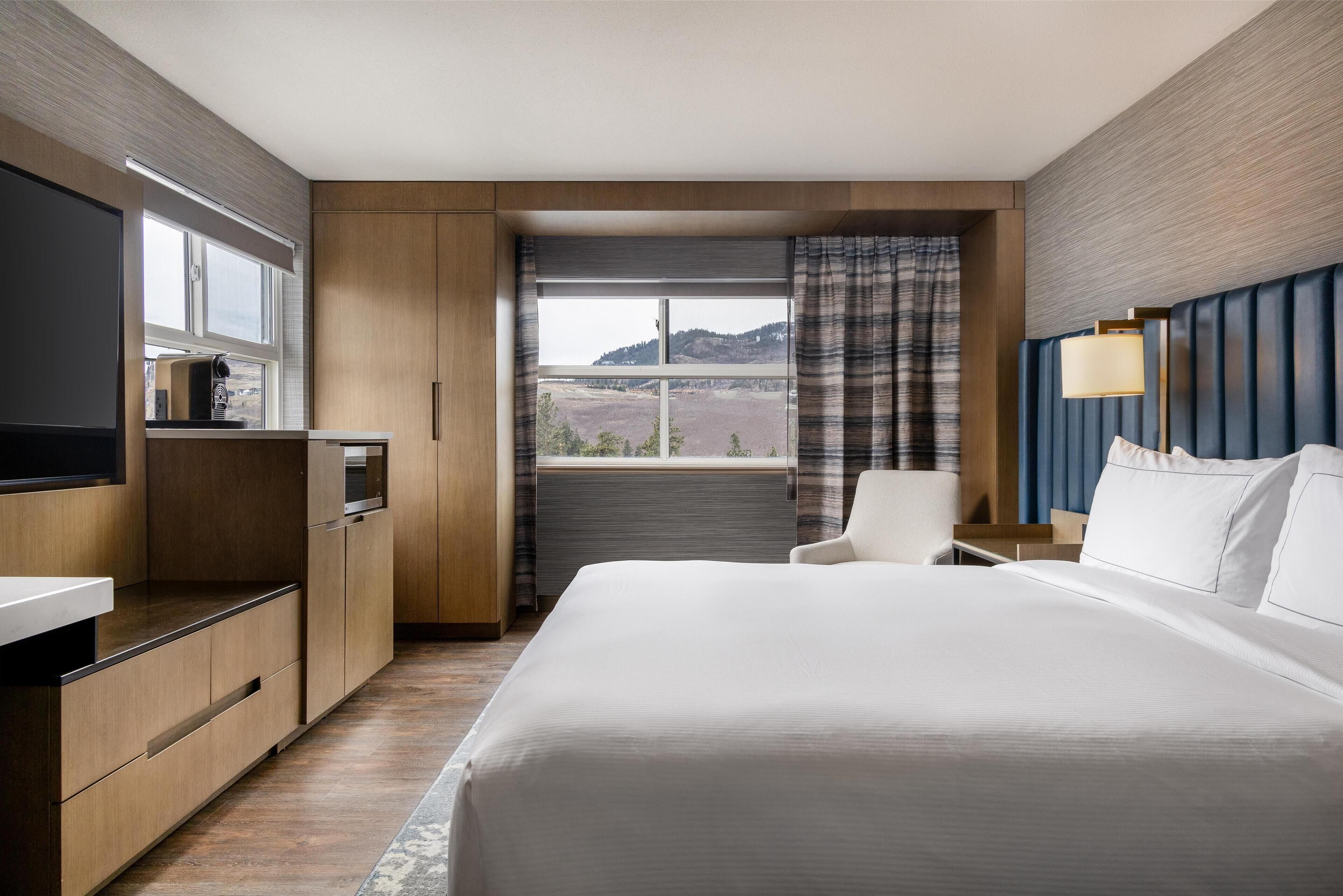 Habitación de hotel con una cama grande, un escritorio, una silla, un televisor y vistas a las montañas.