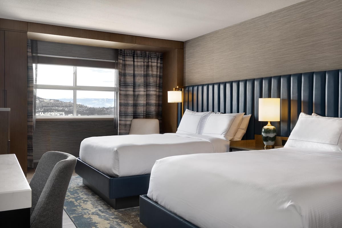 Ett hotellrum med två sängar, ett skrivbord, en stol och utsikt över staden.