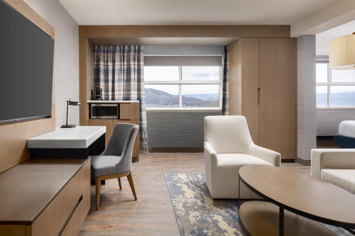 Ett modernt hotellrum med ett stort fönster, ett skrivbord, en stol och en soffa.