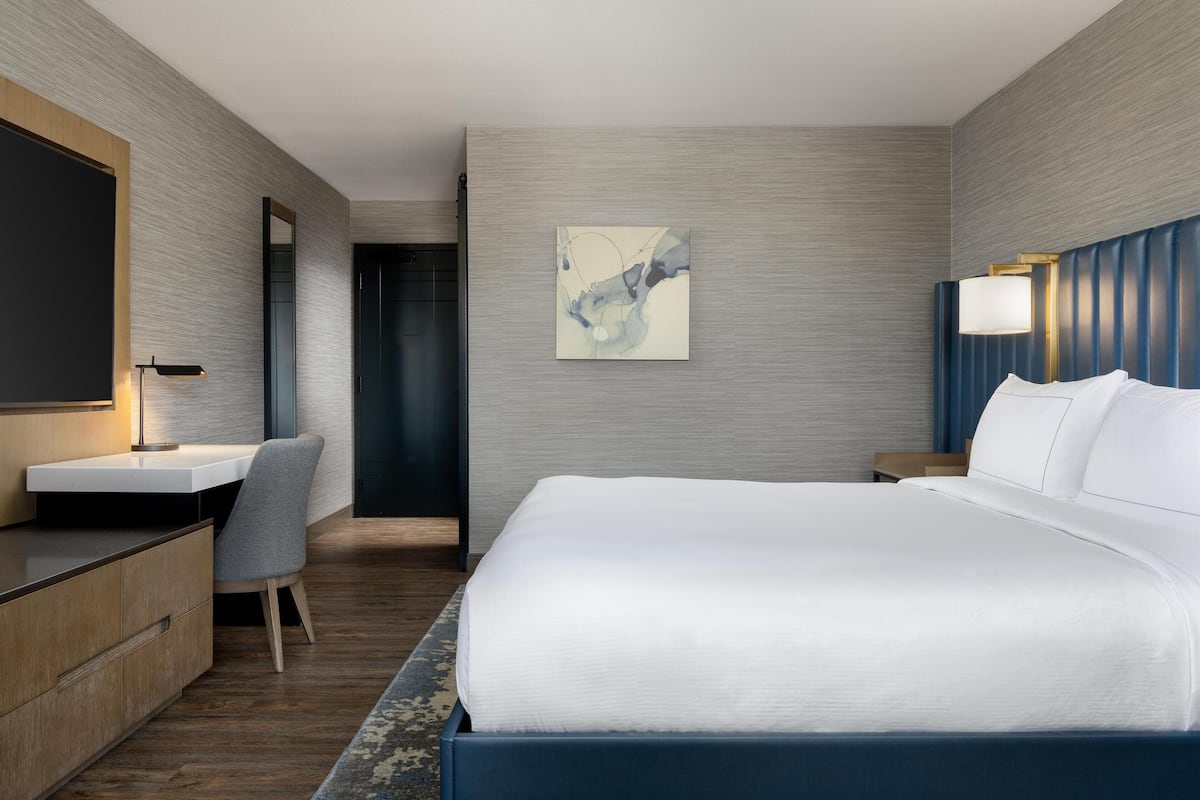 Ett modernt hotellrum med en stor säng, ett skrivbord, en stol och en tavla på väggen.