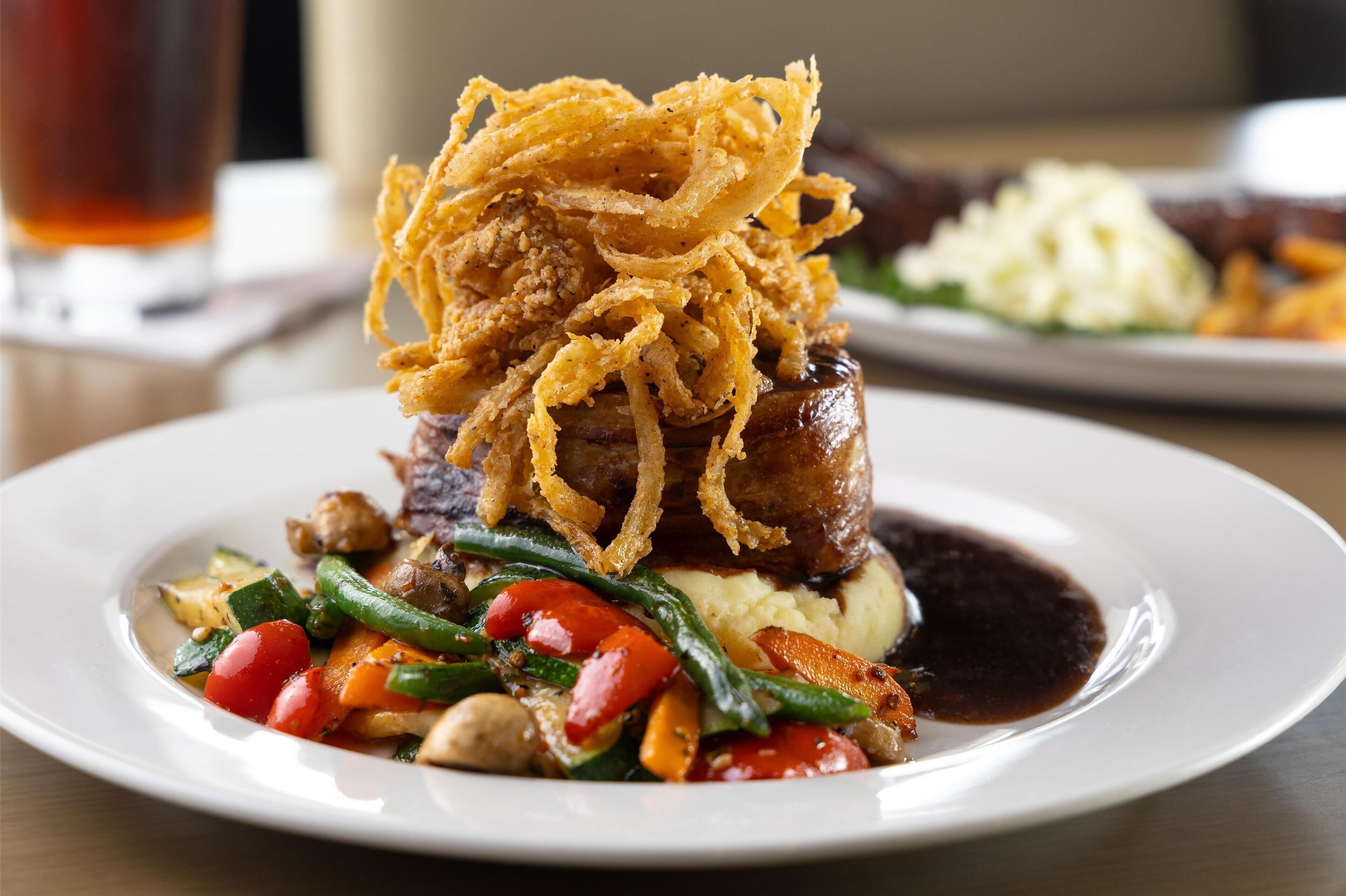 A plate of food with a steak topped with fried onions, green beans, and red peppers.
