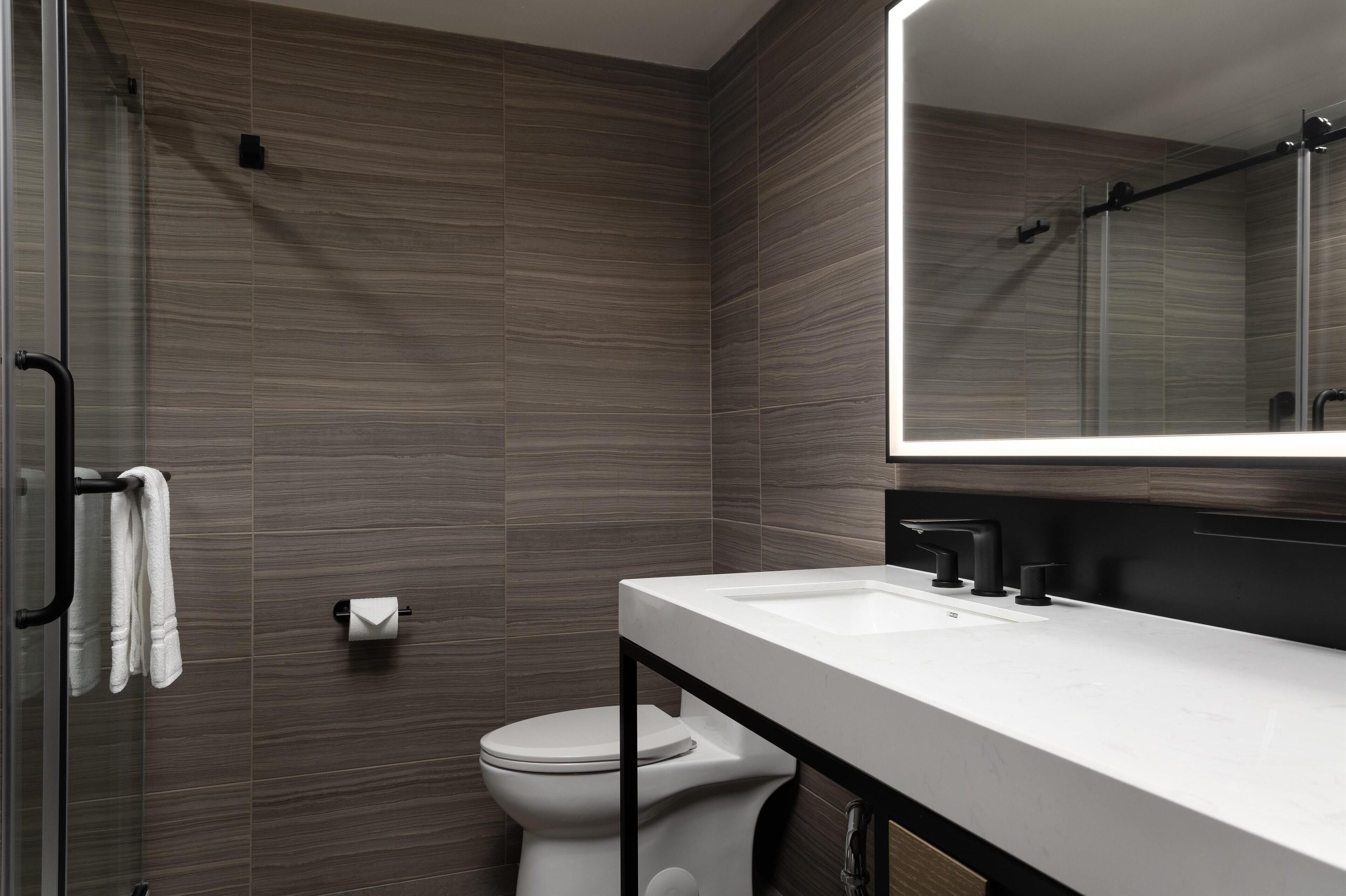 Ein modernes Badezimmer mit Duschkabine aus Glas, einer weißen Toilette und einem weißen Waschbecken mit schwarzem Wasserhahn.