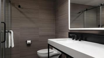 Ein modernes Badezimmer mit Duschkabine aus Glas, einer weißen Toilette und einem weißen Waschbecken mit schwarzem Wasserhahn.
