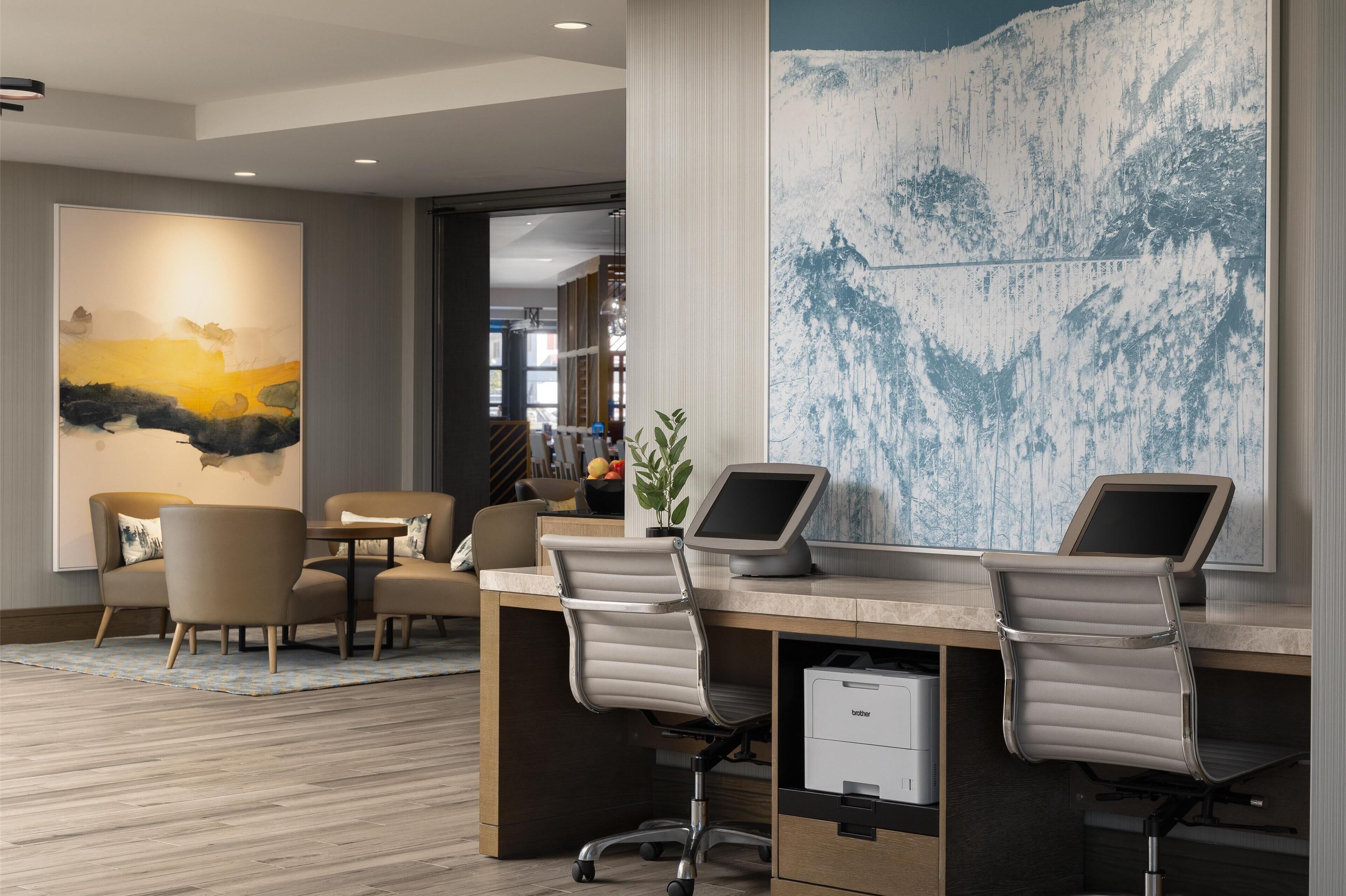 A modern office space with two desks, a large abstract painting, and a view into another room.