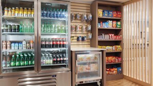 Un espace de libre-service où l’on peut se servir des boissons et des en-cas, avec des distributeurs de boissons réfrigérés, des étagères remplies de diverses boissons et en-cas, et un petit réfrigérateur.