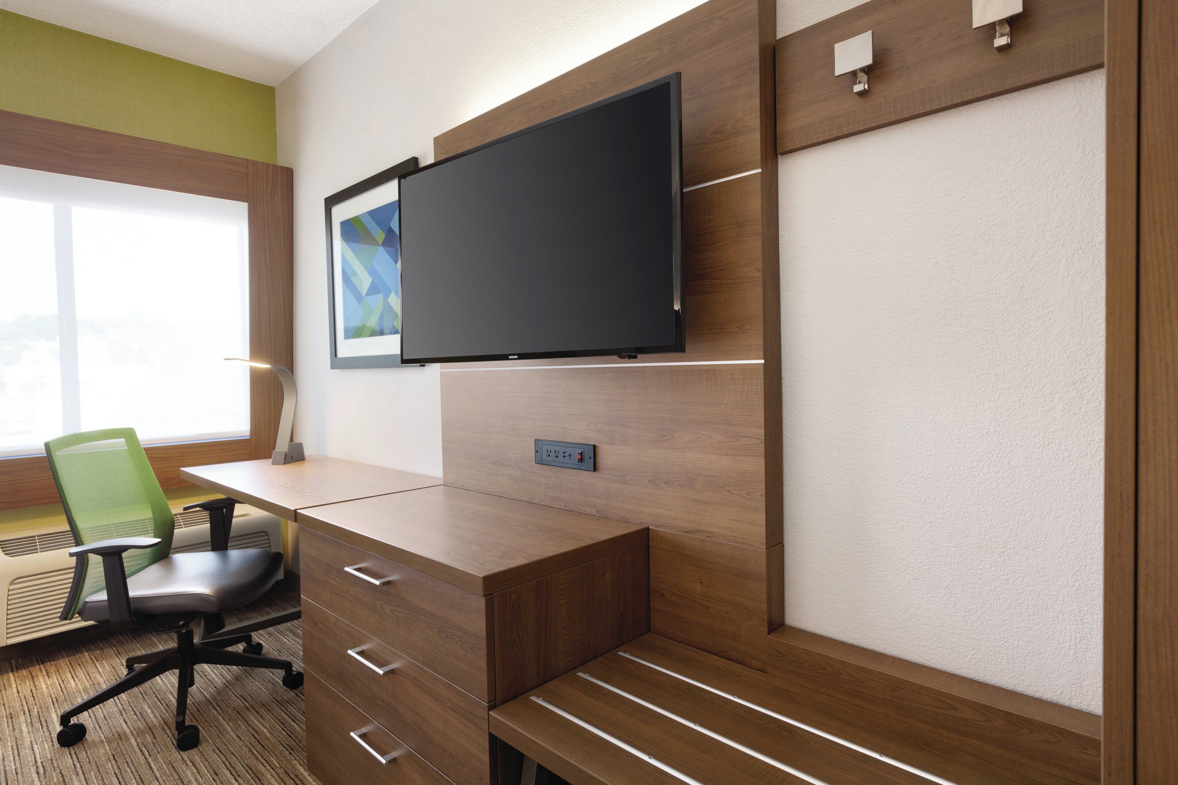 Ein moderner Arbeitsbereich mit einem Holztisch, einem grünen Bürostuhl, einem an der Wand montierten Flachbildfernseher und einem gerahmten Bild.