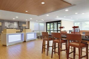 Un hall d’hôtel moderne comprenant un comptoir d’accueil, un bar et un espace détente avec des sièges.