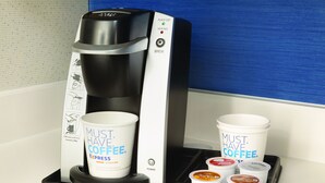 Eine Kaffeemaschine mit Tassenhalter und einer Auswahllade für Kaffeekapseln.