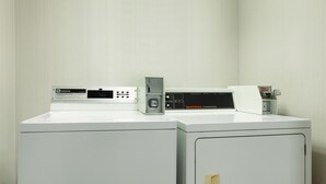 Un espace buanderie équipé de deux machines à laver et d’un sèche-linge, doté de panneaux de commande et d’un distributeur d’eau.