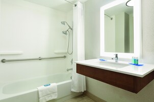 Un baño moderno con bañera, ducha, tocador con espejo y perchero para toallas.