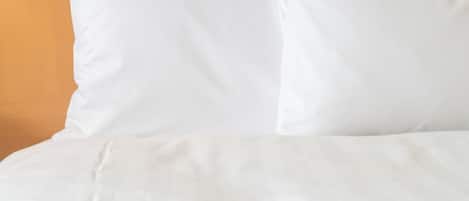 A bed with white bedding and pillows against a wooden headboard.