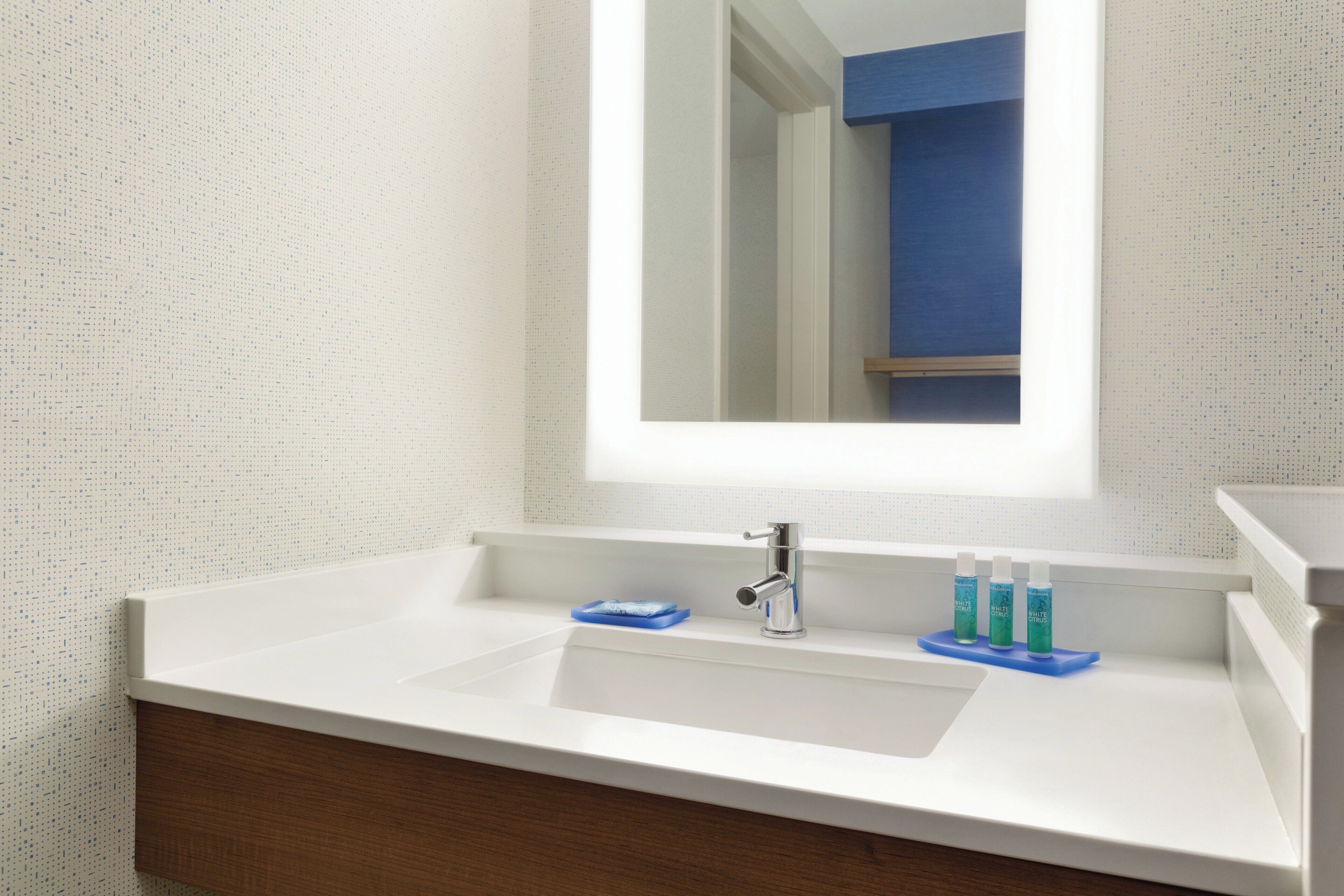 Un baño con un lavamanos blanco, un espejo y un jabonera azul.