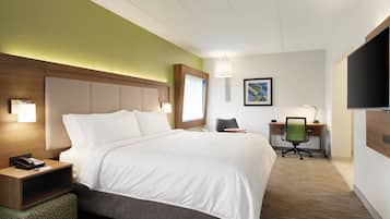 A hotel room with a bed, bedside table, lamp, desk, chair, and TV.