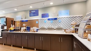 Una barra de desayuno con diversas opciones de comida, incluyendo cereales y alimentos calientes, y un cartel que indica un desayuno exprés.