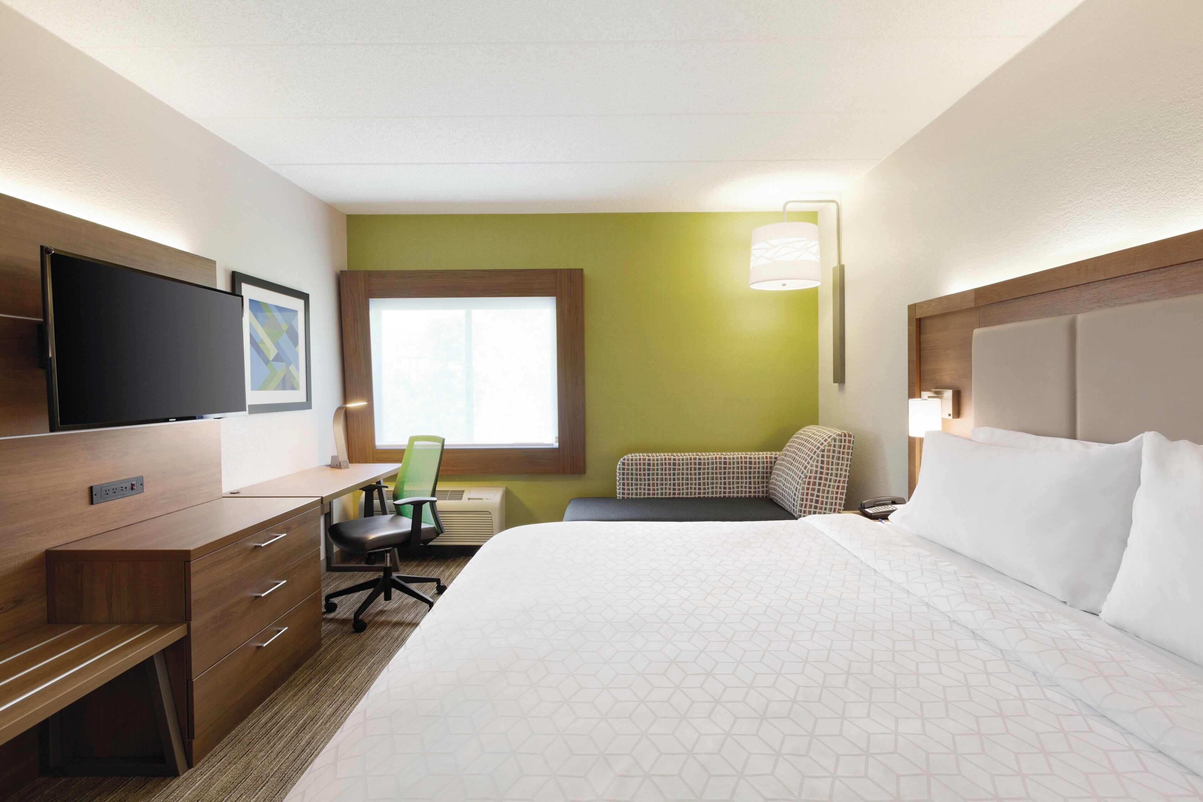 A hotel room with a bed, desk, chair, television, and window.