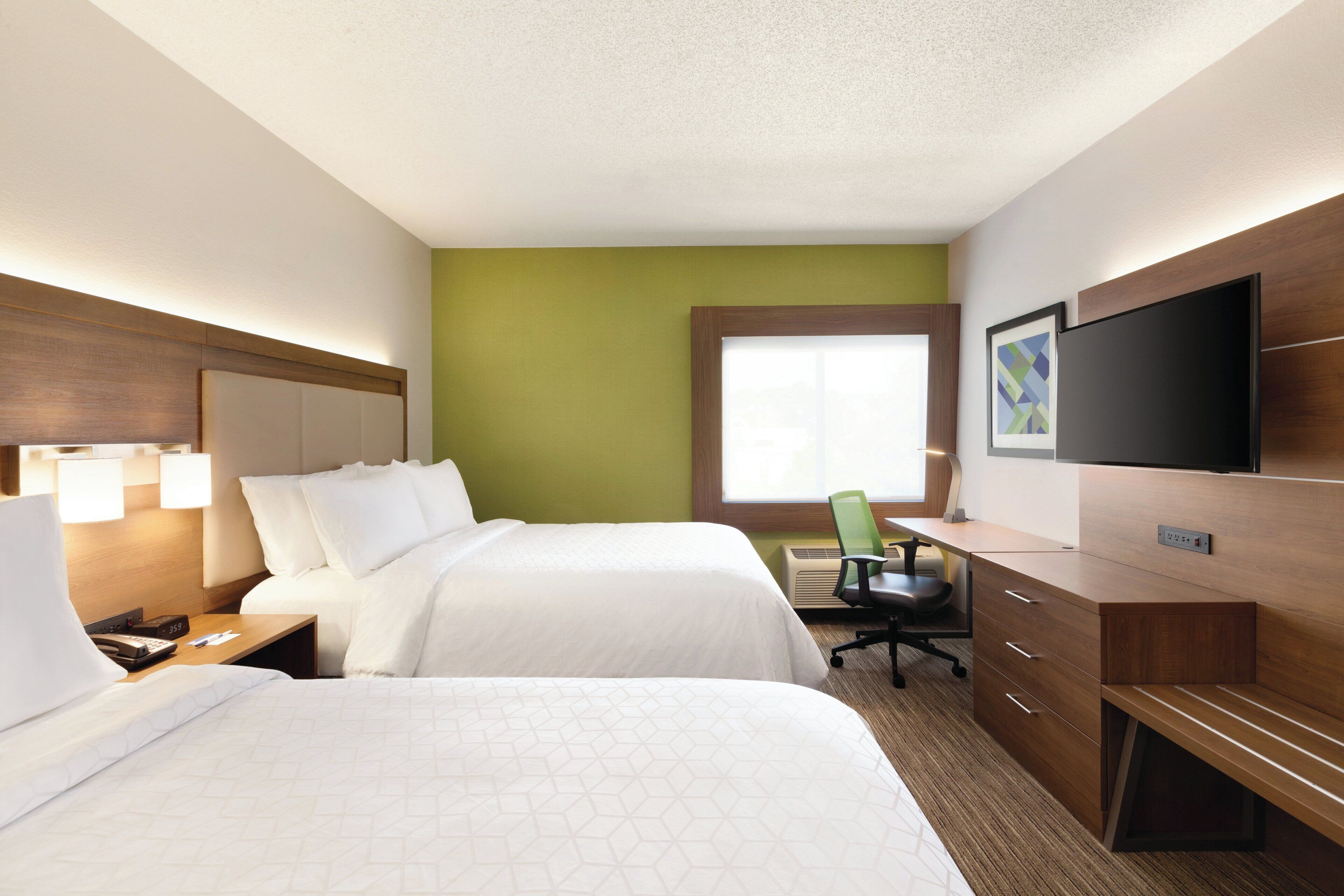 A hotel room with two beds, a desk, a chair, a TV, and a window.