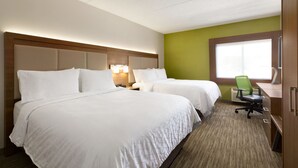 Ein Hotelzimmer mit zwei Betten, einem Schreibtisch, einem Sessel und einem großen Fenster.