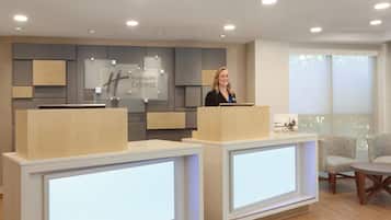 A reception desk area with a Holiday Inn Express sign, a modern design with wood and grey panels, and a large window providing natural light.
