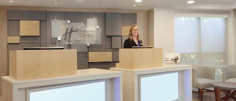 A reception desk area with a Holiday Inn Express sign, a modern design with wood and grey panels, and a large window providing natural light.
