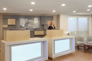 A reception desk area with a Holiday Inn Express sign, a modern design with wood and grey panels, and a large window providing natural light.