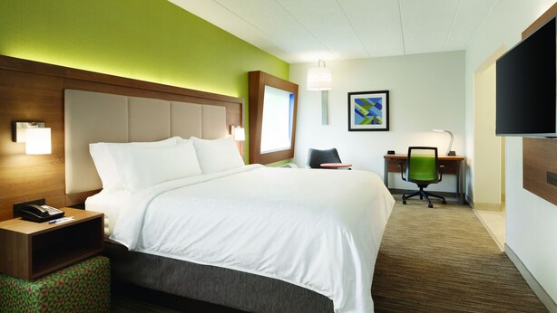 Ein Hotelzimmer mit einem großen Bett, einem Schreibtisch mit Stuhl, einem Telefon und einem Fernseher an der Wand.