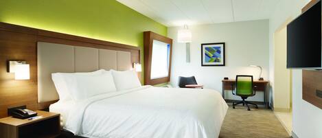 A hotel room with a large bed, a desk with a chair, a telephone, and a TV on the wall.