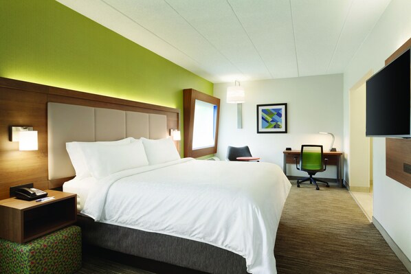 Ein Hotelzimmer mit einem großen Bett, einem Schreibtisch mit Stuhl, einem Telefon und einem Fernseher an der Wand.