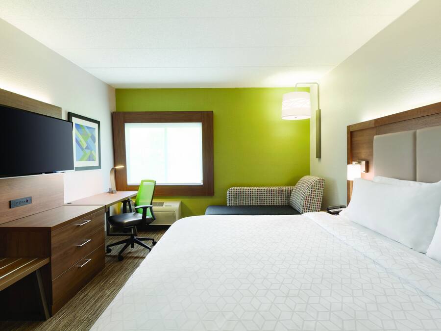 A hotel room with a bed, desk, chair, television, and a window.