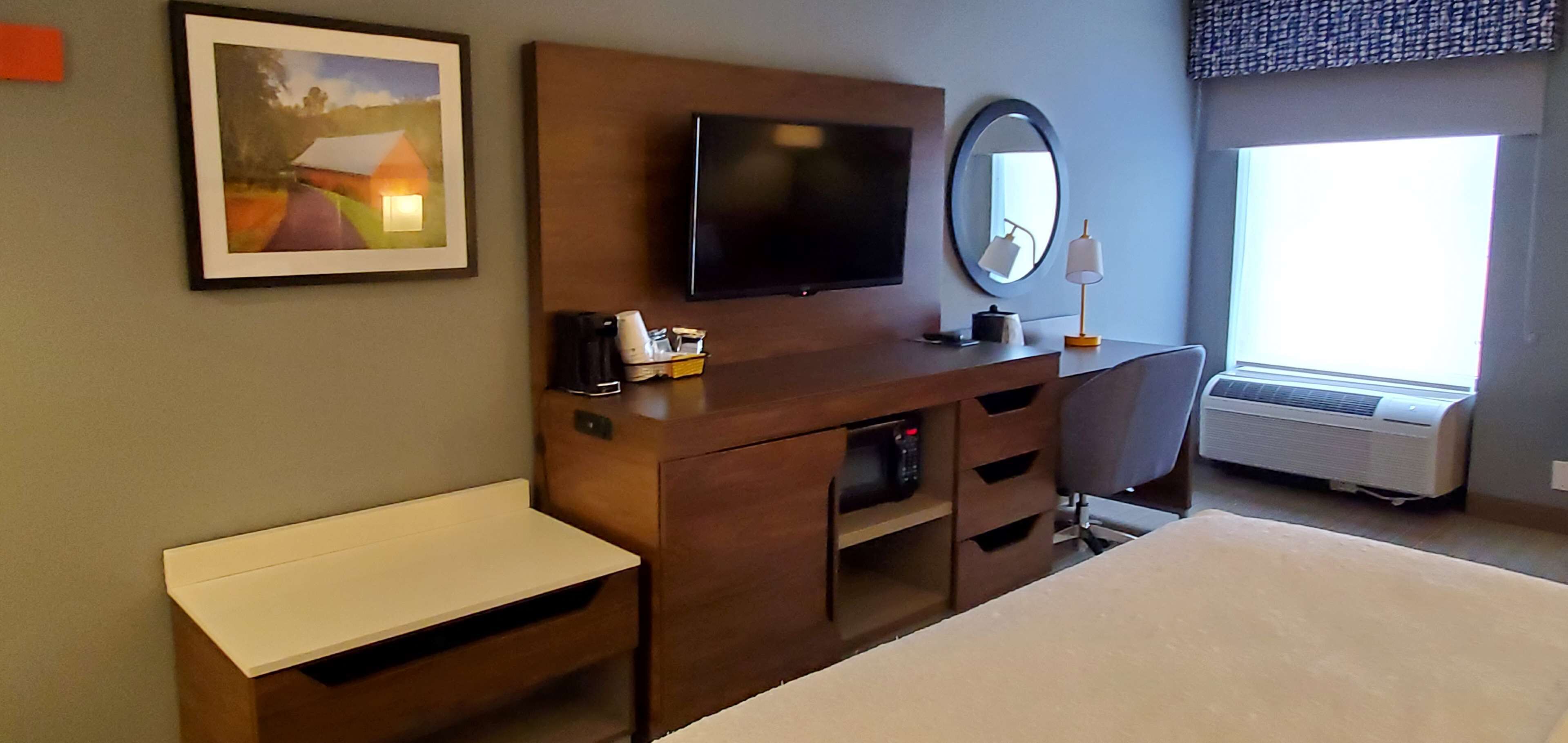 A hotel room with a bed, a TV, a desk, a mirror, and a window.