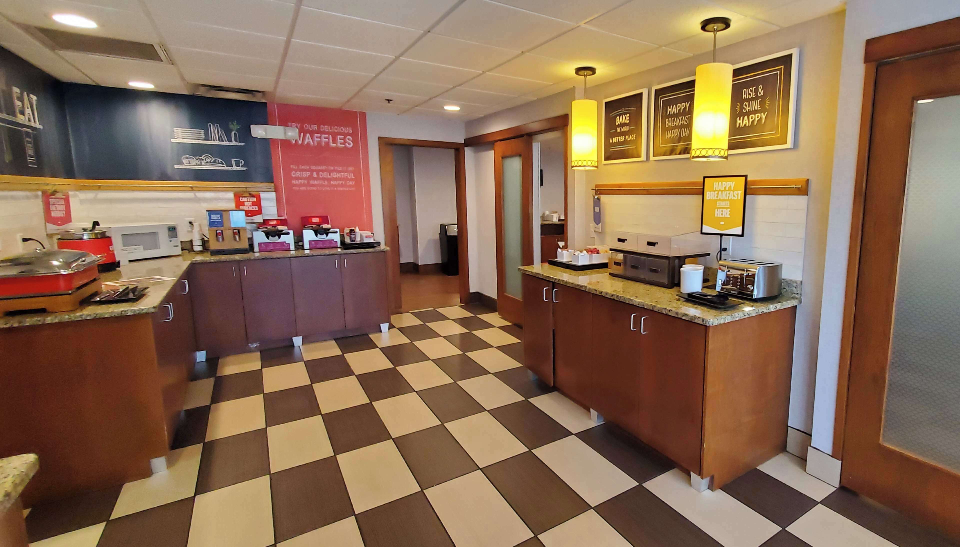 A hotel kitchen with checkered flooring, a waffle station, and various appliances.