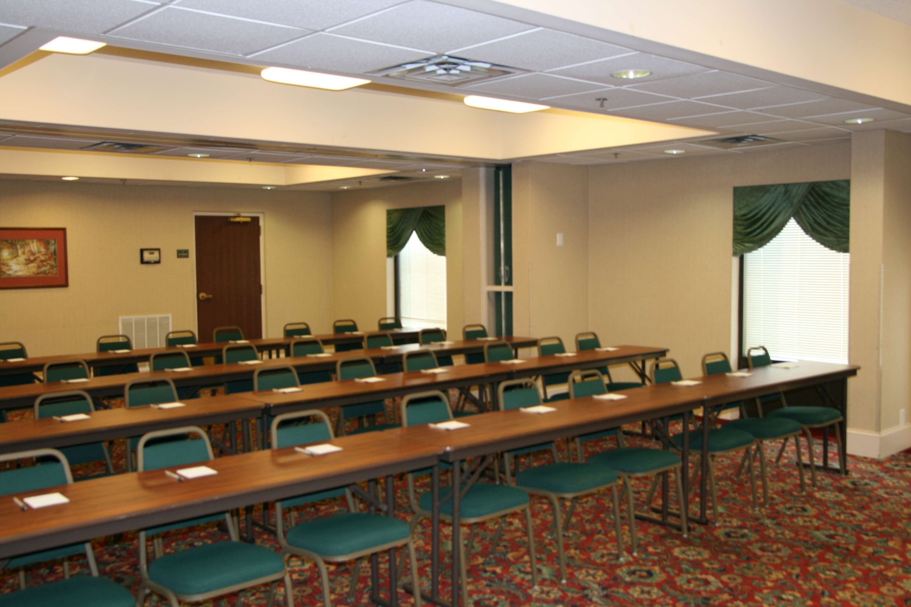 Ein Konferenzraum mit langen Tischen, Stühlen, einer Tür und Fenstern mit Vorhängen.