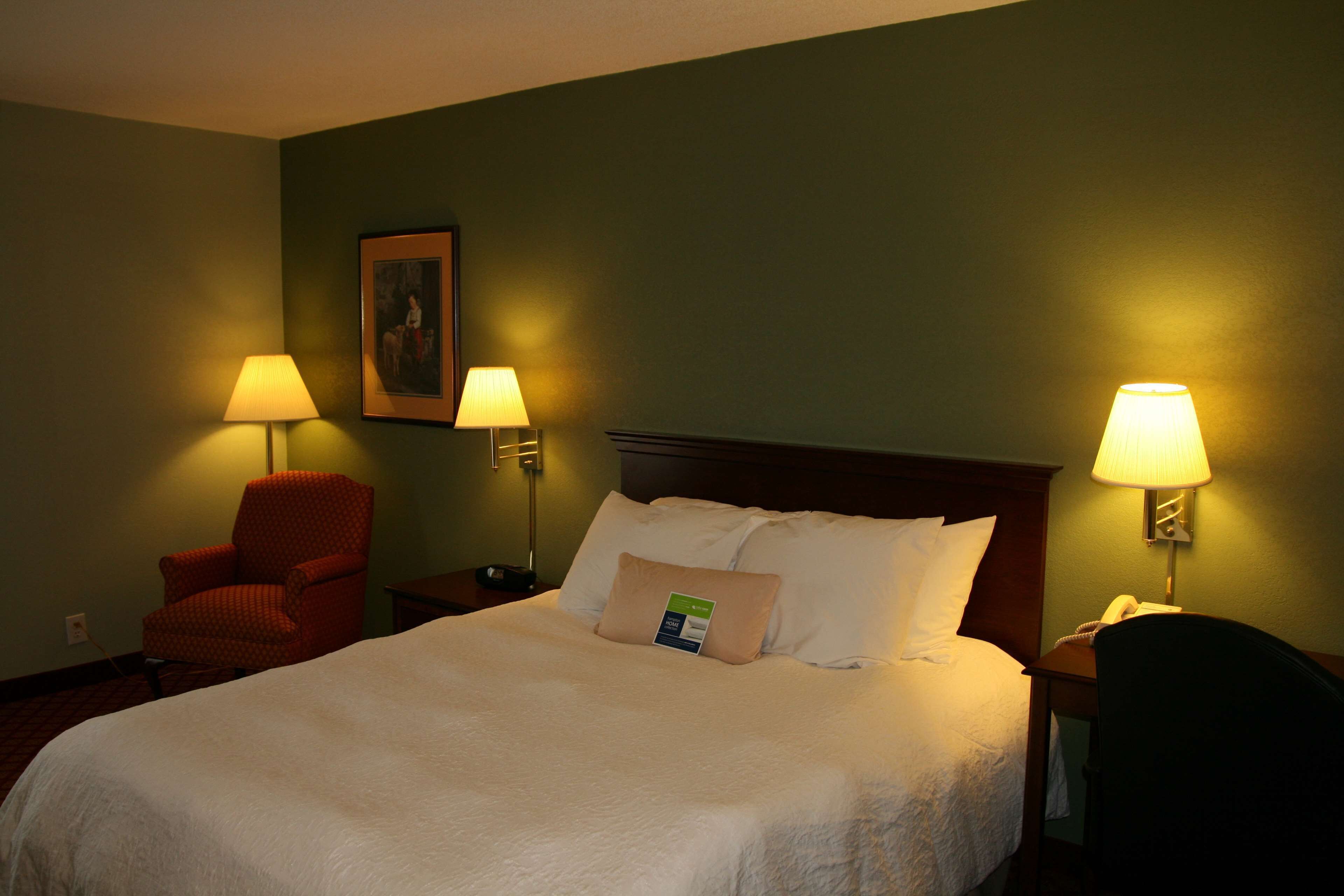 A hotel room with a large bed, two bedside lamps, a chair, and a nightstand with a phone.