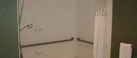 Un baño con paredes de azulejos blancos, una ducha con puerta de cristal, un asidero y un taburete pequeño blanco.