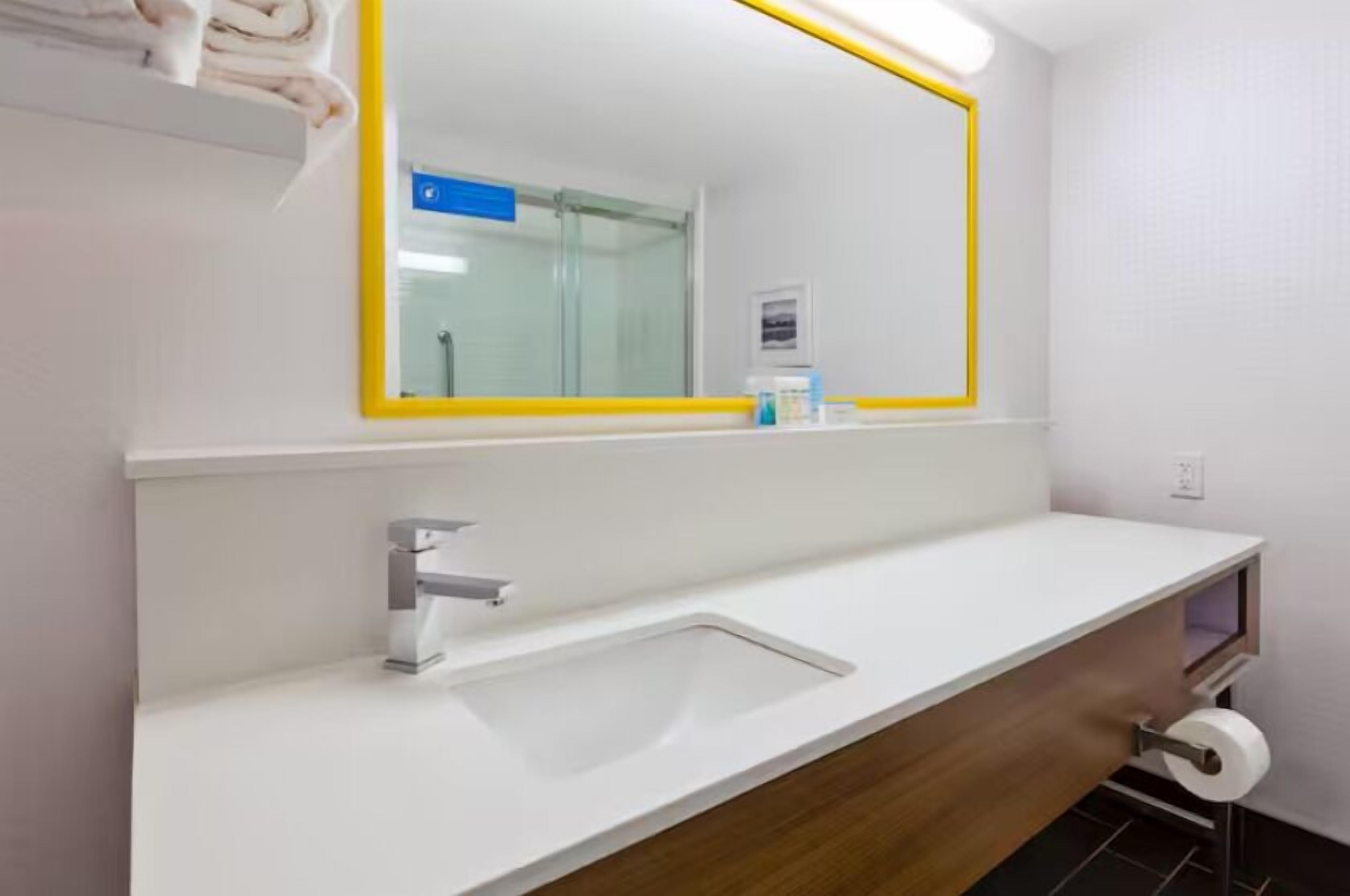 A modern bathroom with a white sink, a mirror with a yellow frame, and a towel rack.