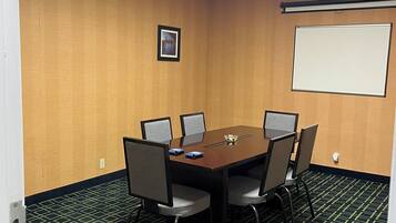 Un salón de conferencias con una mesa rectangular, seis sillas, una pantalla de proyector y un cuadro en la pared.
