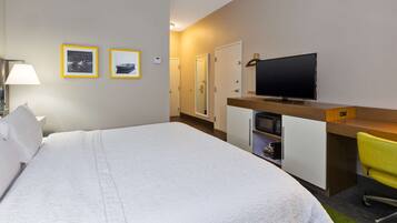 A hotel room with a large bed, a desk with a television, a chair, and two framed pictures on the wall.