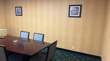 A conference room with a large table, four chairs, two framed pictures on the wall, and a patterned carpet.