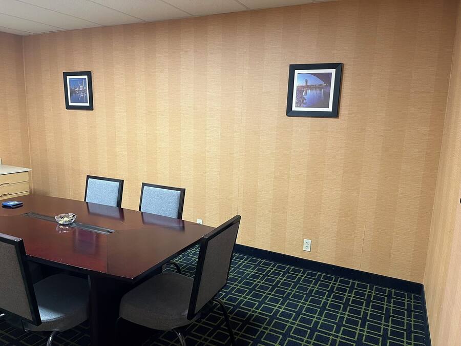 A conference room with a large table, four chairs, two framed pictures on the wall, and a patterned carpet.