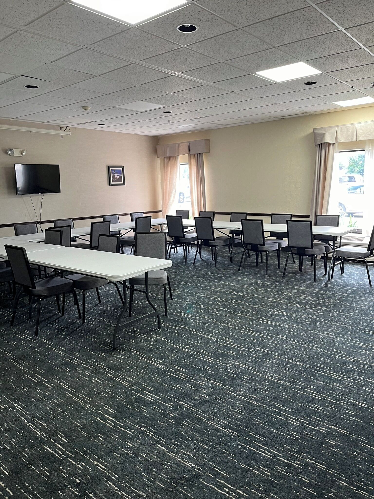 A conference room with multiple tables and chairs, a flat-screen TV mounted on the wall, and a window with curtains.