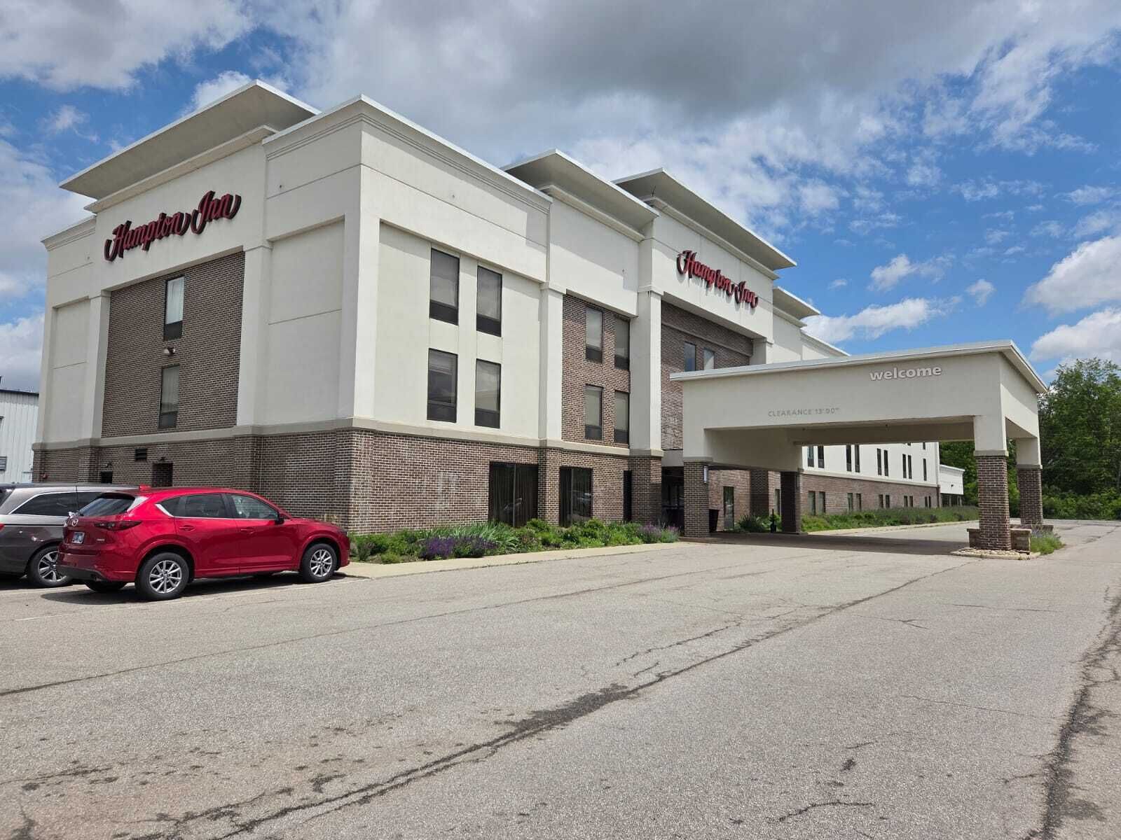 A Hampton Inn hotel with a modern design, featuring a covered entrance and a parking lot.